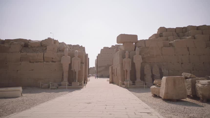 Ancient statues of pharaohs guard a stone pathway through the historic ruins of the Karnak Temple in Egypt