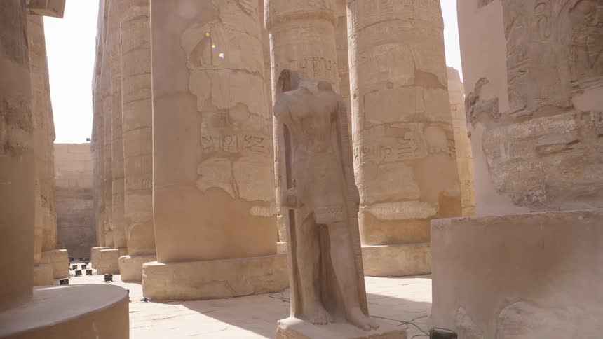 A slow pull-back shot reveals a headless pharaoh statue standing among the grand hieroglyphic columns of the ancient Karnak Temple