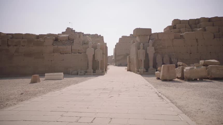 A slow push-in shot reveals an ancient stone walkway flanked by towering pharaonic statues and ruins at the Karnak Temple complex in Egypt