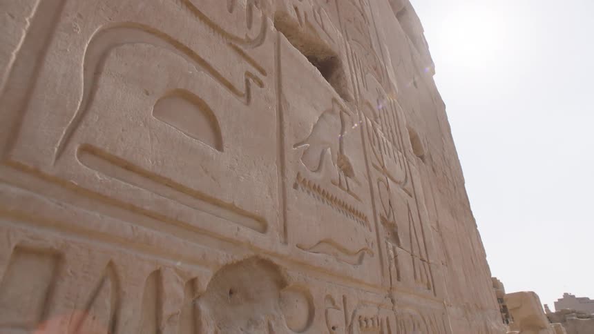 Slow dolly shot reveals ancient Egyptian hieroglyphics carved into a stone temple wall under the bright sun