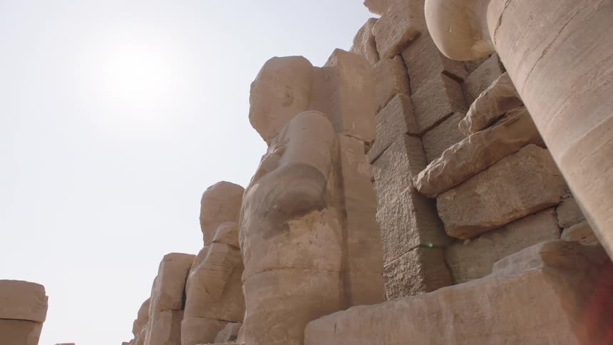 A slow, low-angle tracking shot moves past a row of massive, ancient Egyptian statues at the Karnak Temple Complex