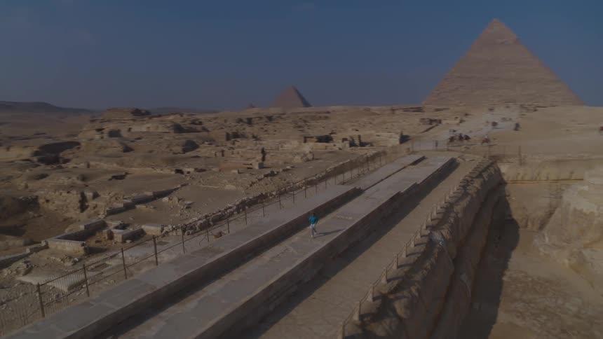 An aerial view reveals a person running from the Great Sphinx towards the pyramids of Giza on a clear day in Egypt