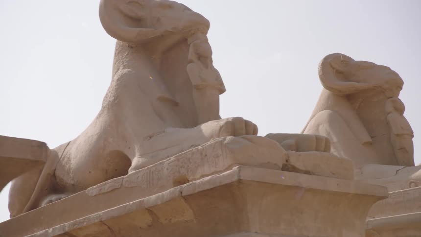 A slow, low-angle tracking shot reveals a row of ancient ram-headed sphinx statues at the Karnak Temple in Luxor, Egypt