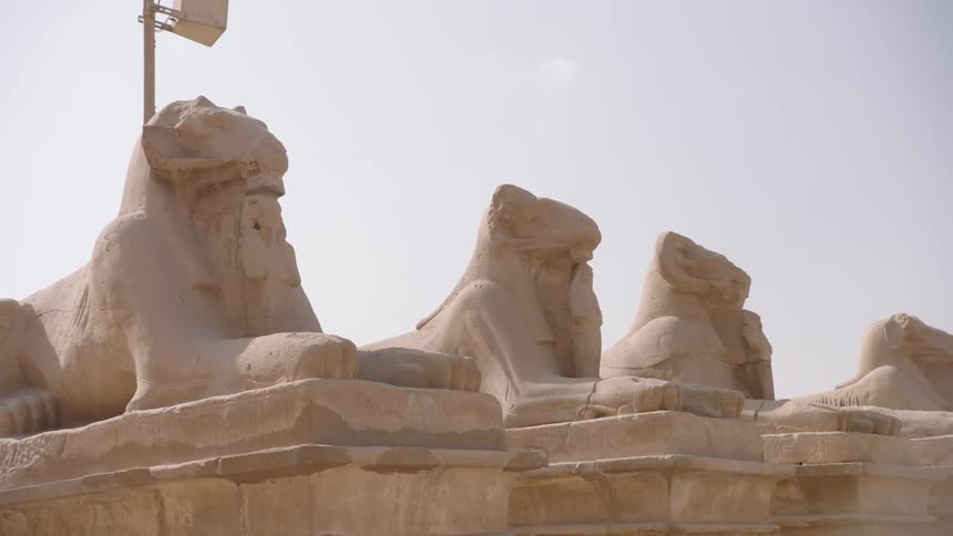 Slow dolly shot past a row of ancient, weathered ram-headed sphinx statues at the Karnak Temple in Egypt