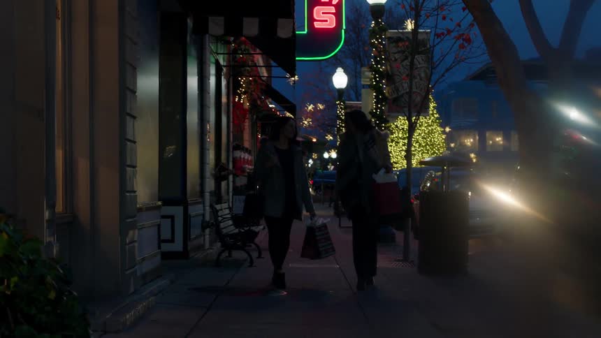 Two women walking down sidewalk at night holding shopping bags