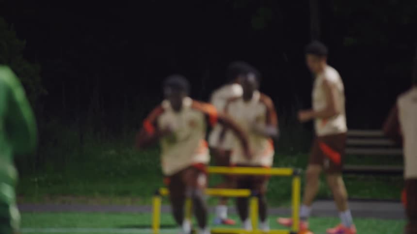 A team of male soccer players jumps over hurdles in slow motion during an agility training session at night