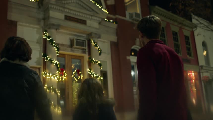 A family approaches a building with christmas lights at night