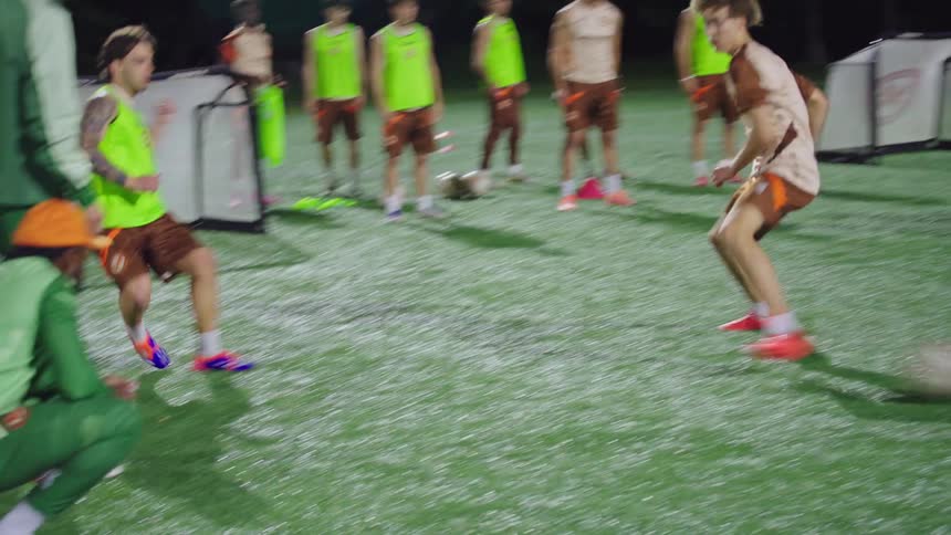 A soccer team in matching uniforms conducts a fast-paced passing drill during a night practice session on an illuminated field