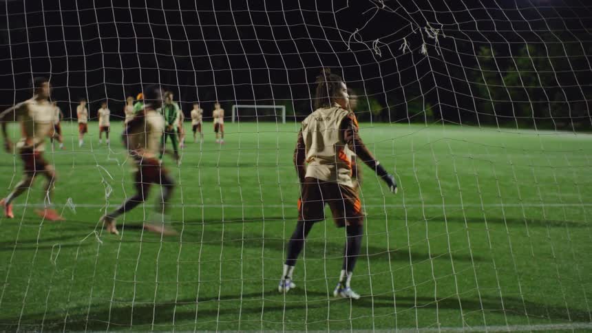 View from behind the net of a soccer goalkeeper making a diving save attempt on a penalty kick during a nighttime practice