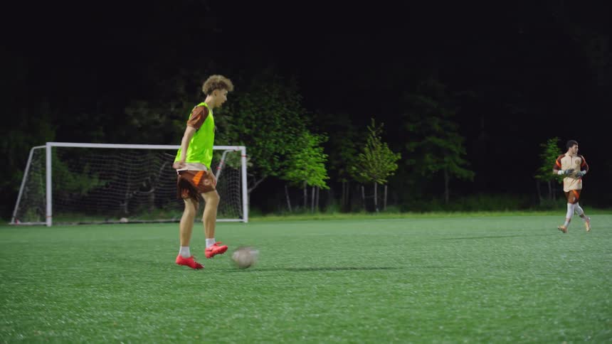 Slow motion tracking shot follows a diverse group of young men during an energetic nighttime soccer practice on a lit field