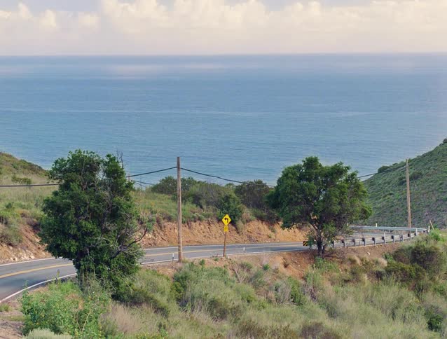 A vintage red convertible drives along a winding coastal highway, overlooking the vast blue ocean