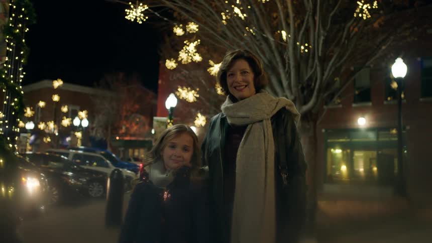 A woman and girl stand on a city street decorated with lights