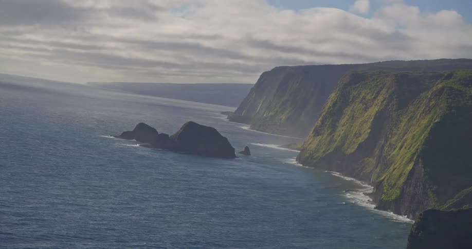 A breathtaking high-angle view of the rugged, green-covered cliffs along a dramatic coastline meeting the vast ocean