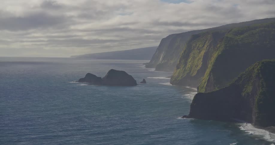 A majestic, wide, static shot of the rugged, green cliffs along the Pololu Valley coastline in Hawaii on an overcast day
