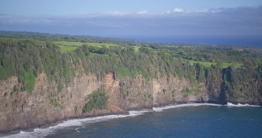 A slow aerial pullback reveals the lush green cliffs along a serene ocean coastline