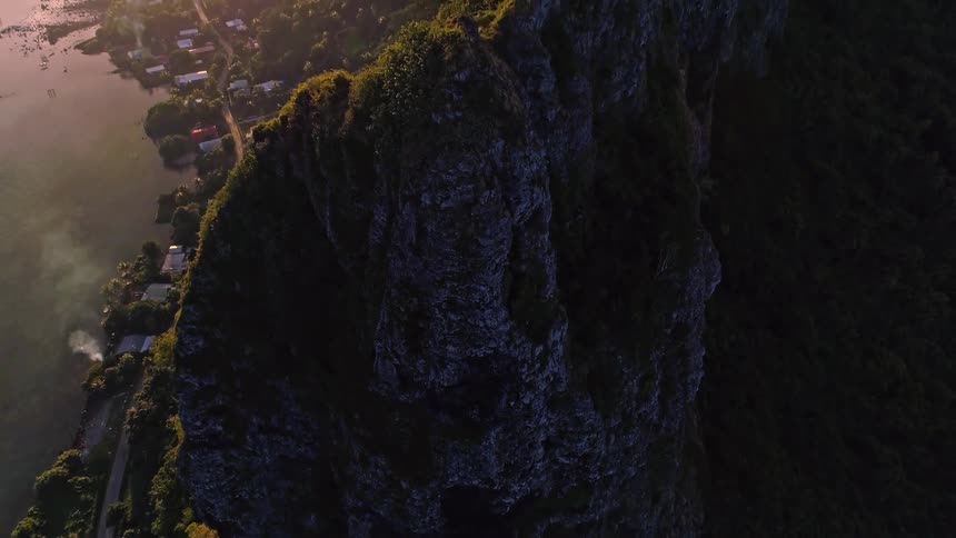 A dramatic aerial reveal of a majestic mountain ridge on a tropical island during a beautiful sunset over the ocean