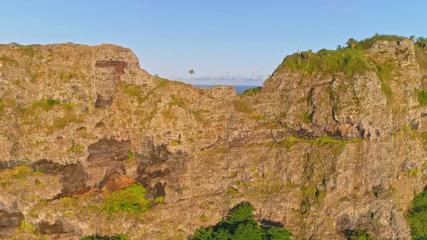 An aerial view flies slowly towards a rugged coastal mountain, revealing a beautiful tropical lagoon and village