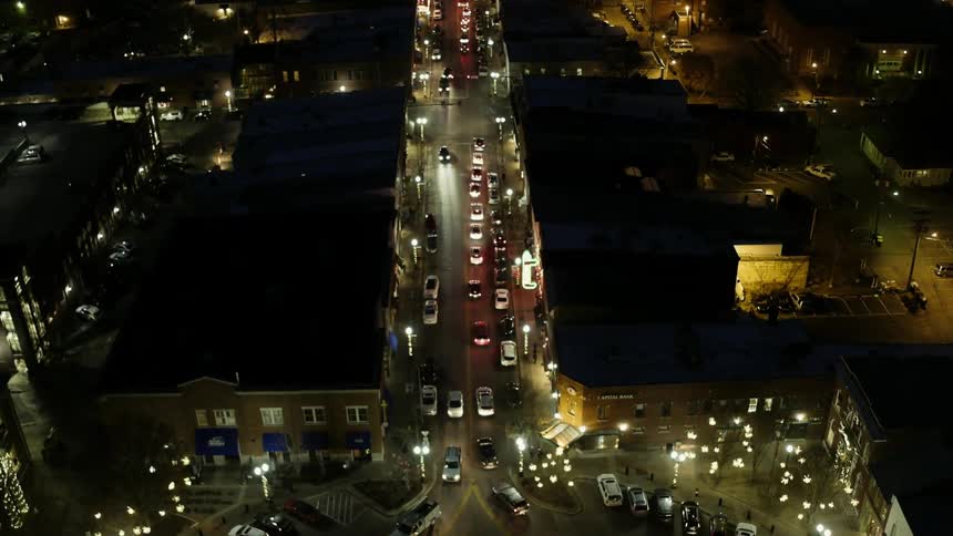Cars traveling on busy city street at night near lit up christmas tree