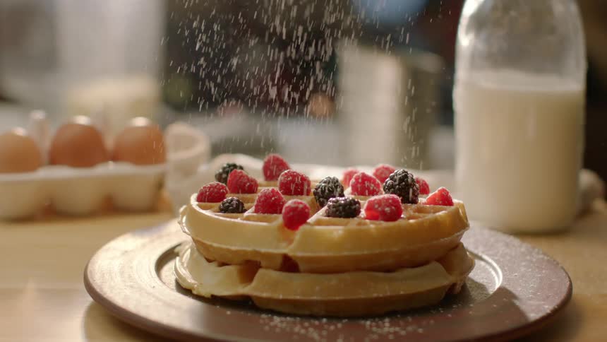 Powdered sugar sprinkling onto a pile of waffles on breakfast table