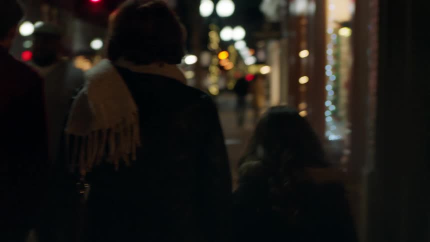A family walks on a city sidewalk with glowing christmas decorations all around
