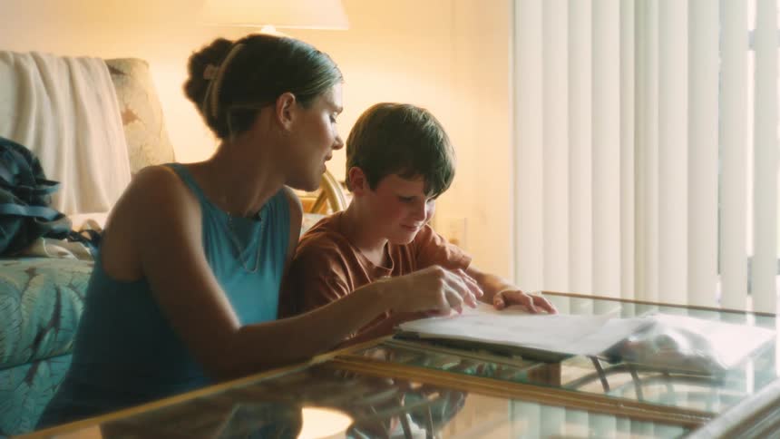 A loving mother watches her son as he happily draws in a warmly lit living room