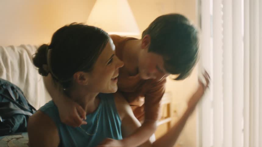 A smiling mother receives a surprise hug and kiss from her affectionate son in their warmly lit home