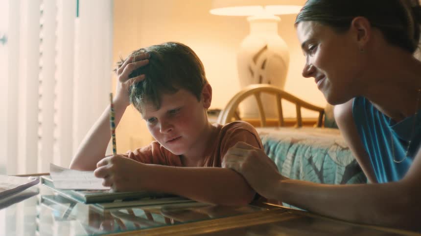 A supportive mother encourages her frustrated young son as he concentrates on his homework at home