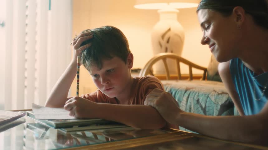 A supportive mother encourages her frustrated young son as he concentrates on his homework at home