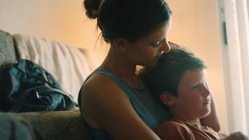 A tender moment between a mother and her son as she holds him close and kisses his head by a sunlit window