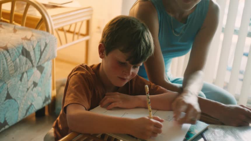 A caring mother kneels down to help her young son with his homework in their cozy, sunlit home