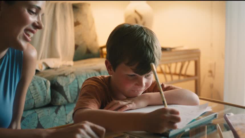 A mother encourages her young son as he works on his homework, and they share a celebratory high-five upon completion