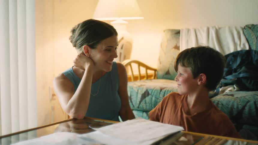 A loving mother proudly watches her son finish his homework, and they celebrate with a slow-motion high-five