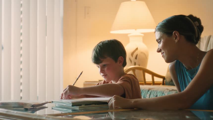A caring mother assists her young son with his homework, guiding him as he writes in his workbook