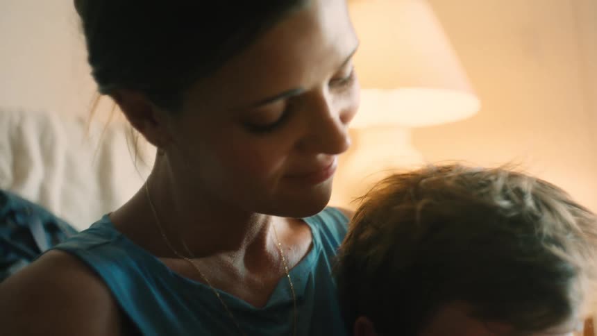 A mother tenderly caresses her young son's hair and pulls him into a loving embrace in a warmly lit home