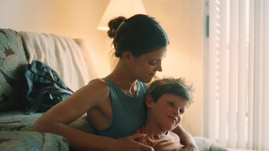 A loving mother tenderly embraces her son, running her fingers through his hair and kissing his head in a quiet moment at home