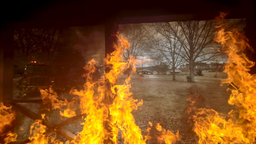 Firefighters and emergency vehicles respond to a structure fire, viewed from within the blaze