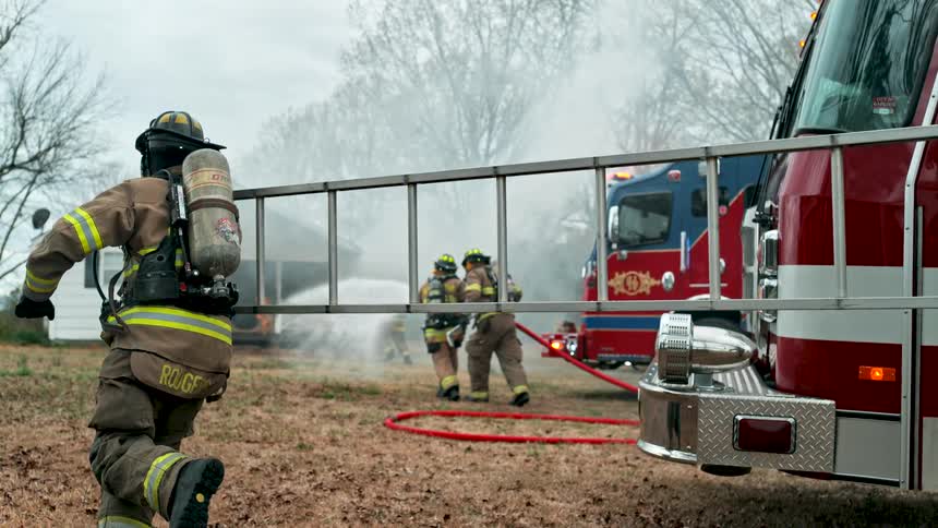 Heroic firefighters in full protective gear battle a blazing house fire with a fire truck nearby in a dramatic slow-motion scene