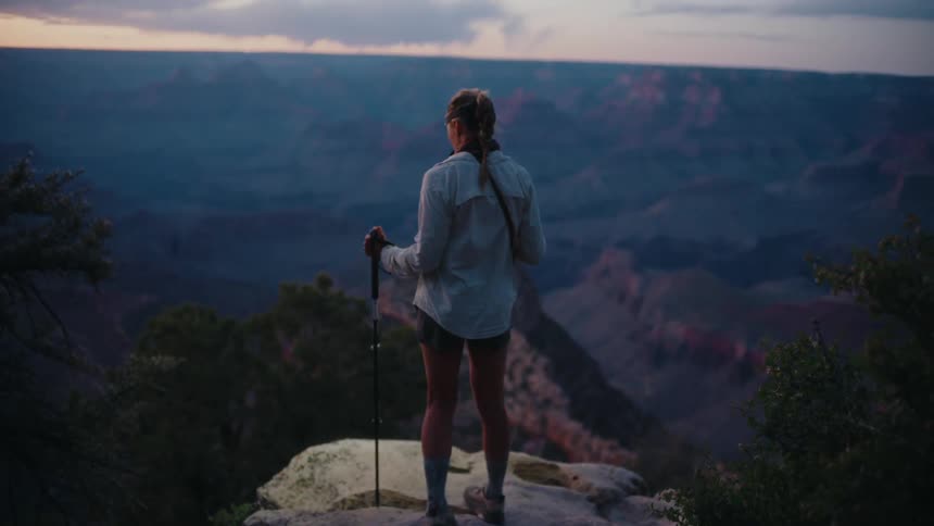 A hiker with trekking poles walks to a rocky outlook in slow motion and takes in the breathtaking view of the Grand Canyon at sunrise