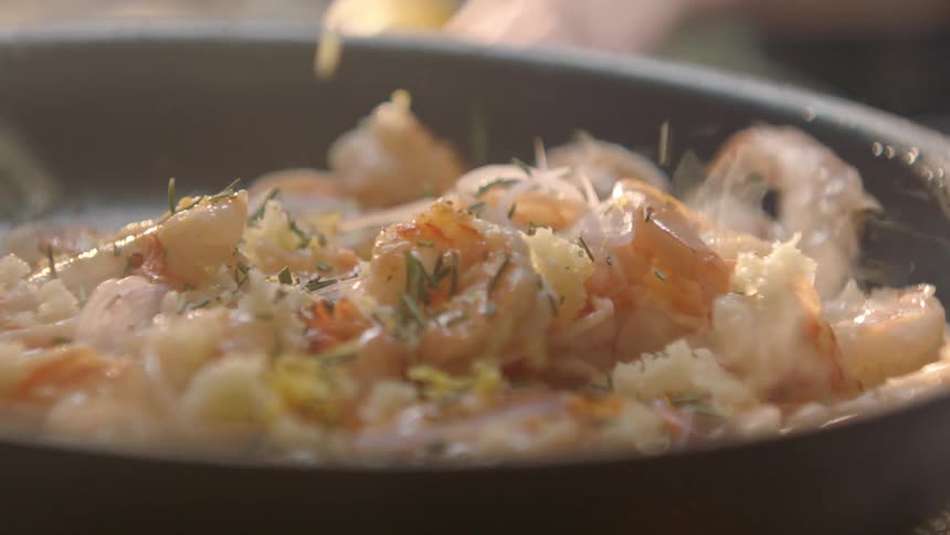 Spices are dropped on shrimp cooking on a pan