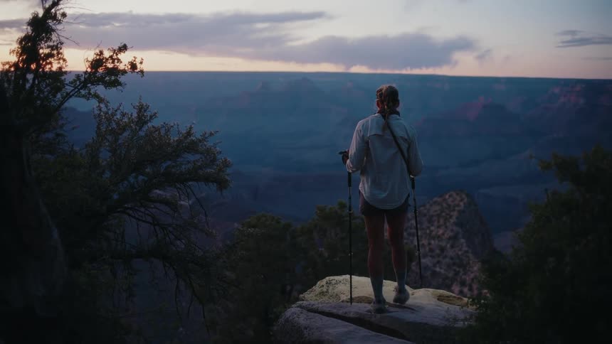A female hiker reaches a rocky overlook and pauses to admire the majestic sunrise over the vast Grand Canyon