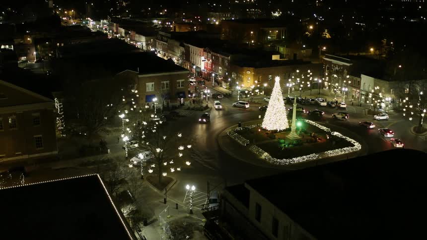 Vehicles travel in a roundabout with a lighted tree at the center