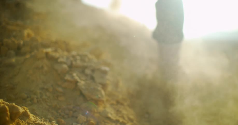 A man kicks up dirt and dust while walking outdoors in boots