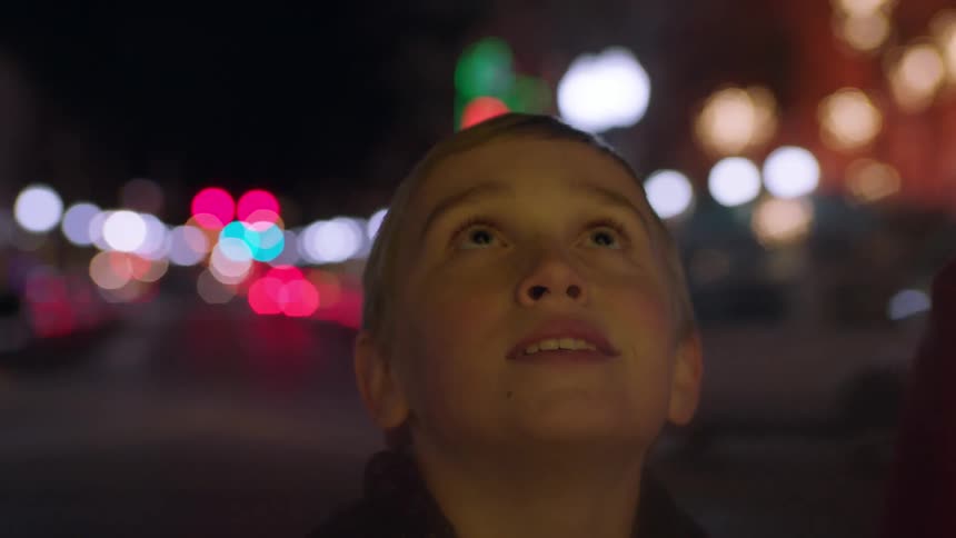 Child standing in the middle of a city at night looking up