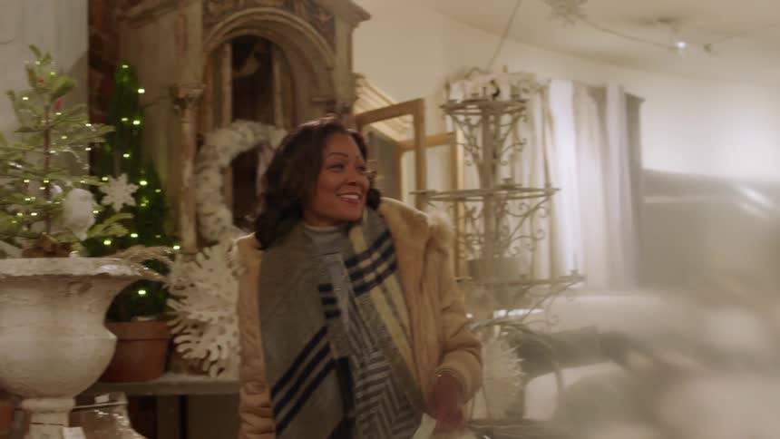 A woman in a gold jacket picks up an item near a tree