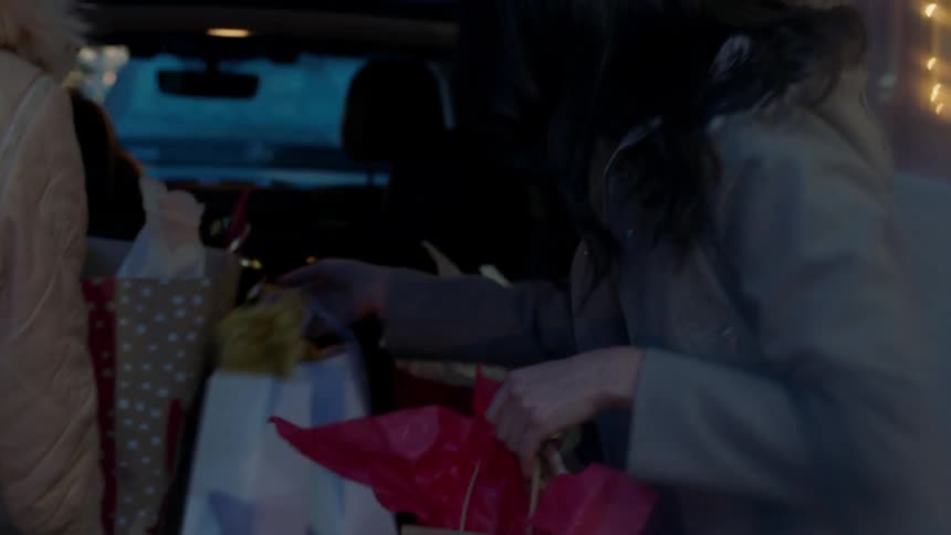 Two women put shopping bags in back of car at night