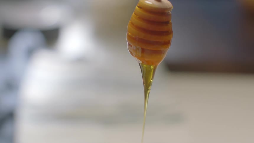 A dripping wand is held over a jar of honey