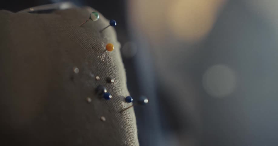 A hand pulls a yellow-headed sewing pin out of a fabric pincushion in slow motion