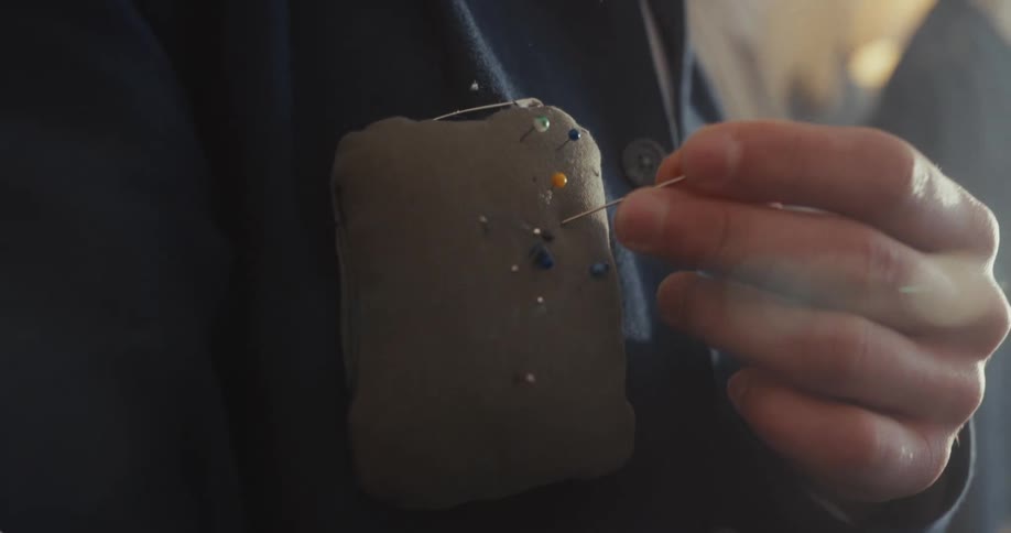 A tailor carefully places a pin into a pin cushion attached to their jacket in a design studio