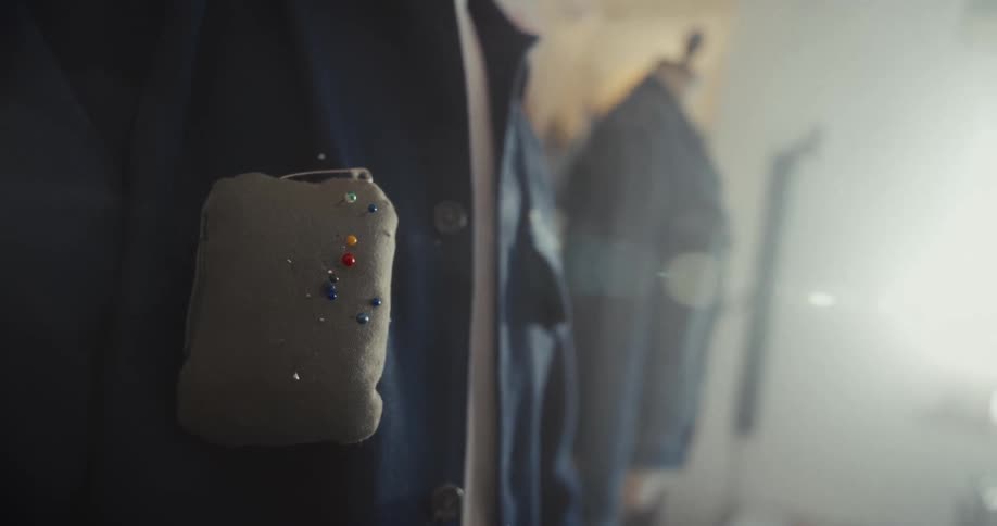 A close-up of a fashion designer's jacket with a pincushion, as they carefully select a pin in their workshop
