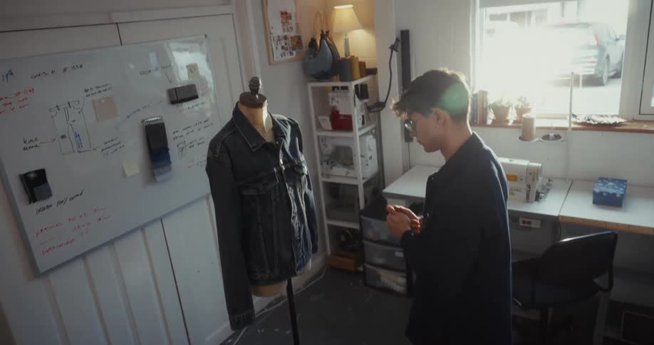 Creative fashion designer adjusts a denim jacket on a dress form in their sunlit workshop